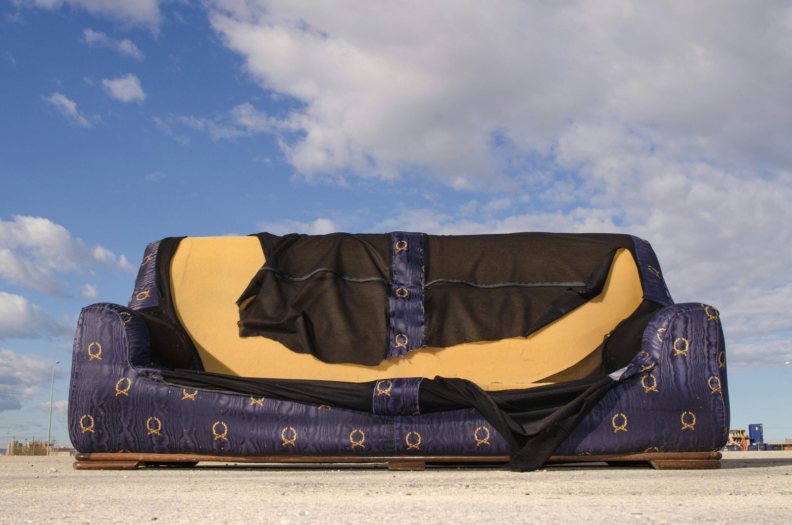 A worn-out sofa left on an empty urban street, highlighted against a blue sky with clouds.