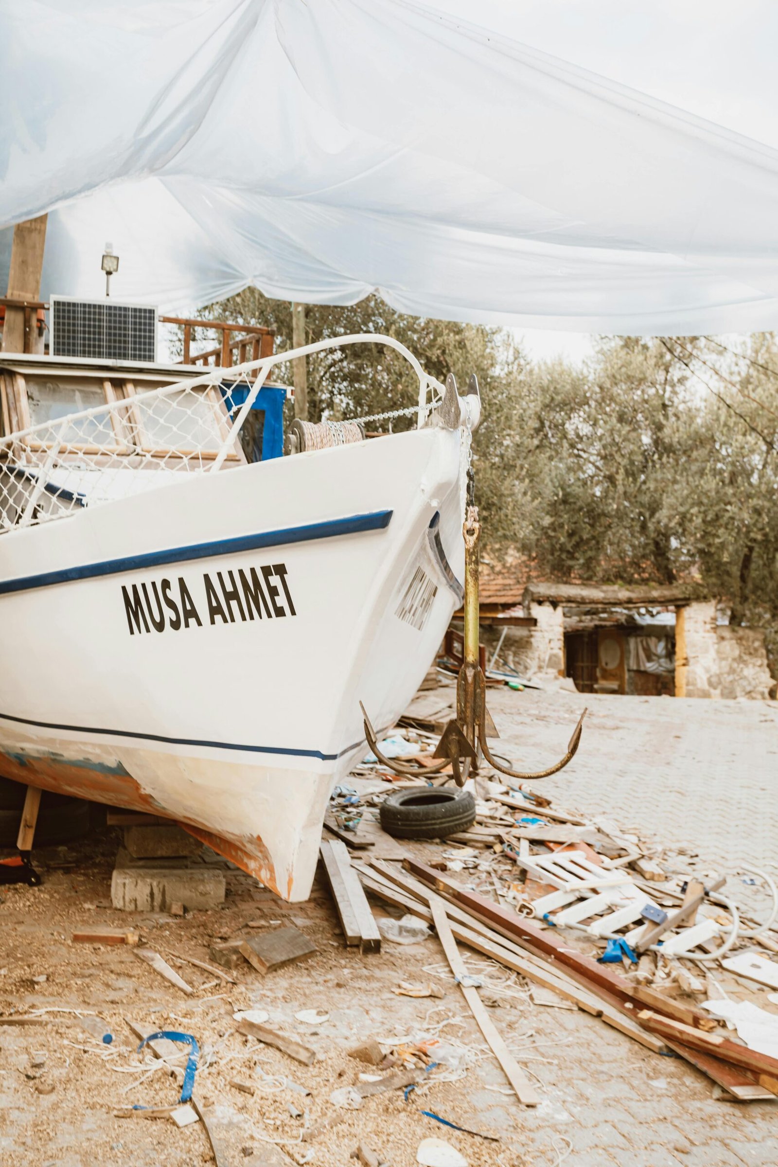 A boat named 'Musa Ahmet' rests on land, surrounded by debris, showcasing an outdoor, rustic scene.