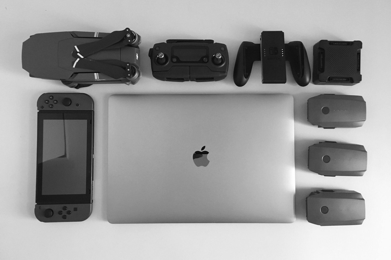 A black and white flat lay of various modern tech gadgets including a laptop, drone, and gaming device.